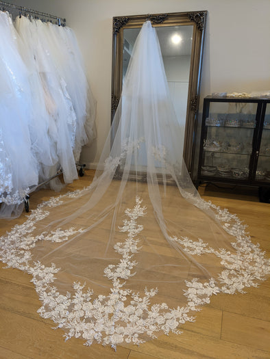 A close-up view of a lace veil adorned with intricate sequined patterns. The delicate fabric features floral designs interwoven with tiny, shimmering sequins, giving it a sparkling and elegant appearance