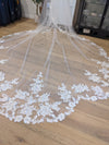 "Close-up of a delicate lace veil with a scalloped edge. The veil is decorated with intricate floral patterns and adorned with sequins for a touch of sparkle."